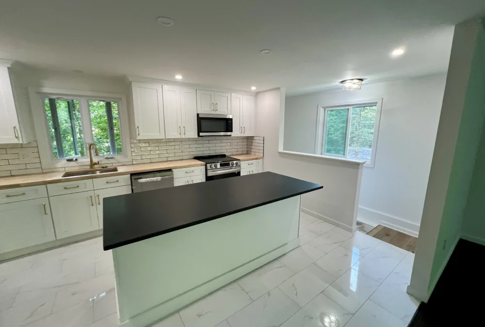 Modern kitchen featuring white cabinetry, black countertop island, stainless steel appliances, and large windows overlooking greenery